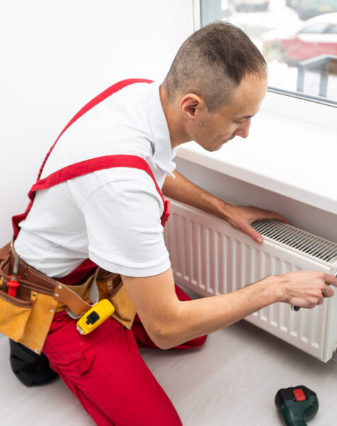 A male plumber installs a radiator in the heating system of an apartment. Guy in overalls and a gas wrench. A male plumber installs a radiator in the heating system of an apartment. Guy in overalls and a gas wrench. High quality photo